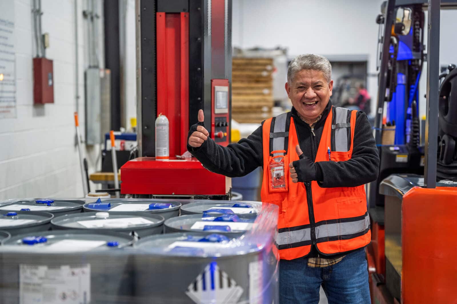 A man in an orange vest stands beside a stack of cans.