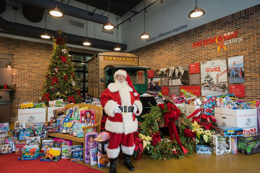 Santa Claus standing in the lobby of an office surrounded by toy drive donations