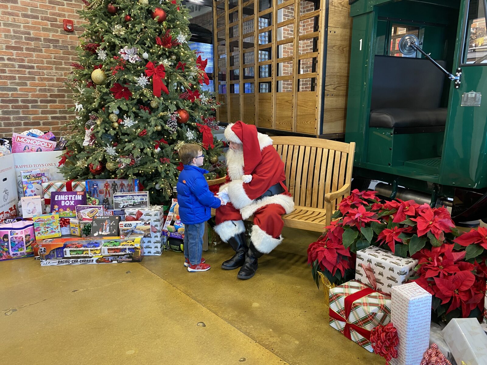 Santa Claus sits on a bench and holds hands with a little boy in a blue jacket