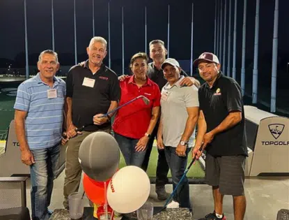 Group of people standing together holding golf clubs.