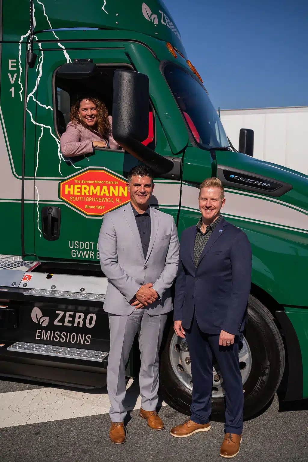 Two men standing in front of a truck with a female inside the truck